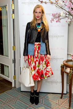 a woman standing in front of a white wall holding a purse and wearing a black leather jacket