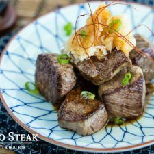 a white plate topped with meat covered in sauce and garnished with scallions