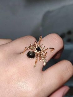 Embrace the captivating allure of the Wire Wrapped Spider Ring & Brooch, a stunning piece that brings together intricate craftsmanship and a bold statement design. This piece can be worn as a ring or a brooch, showcasing a meticulously wire-wrapped spider made from gold-plated copper wire. The spider's body is adorned with a 3mm black sandstone and a 6mm gold obsidian, creating a mesmerizing contrast of texture and depth. Each piece is fully customizable in size, ensuring a perfect fit for your Halloween Wire Rings, Goth With Gold Jewelry, Black Metal Rings For Halloween, Gothic Party Ring Jewelry, Gothic Party Ring, Unique Black Rings For Halloween, Unique Black Halloween Rings, Black Metal Brooch Jewelry, Gothic Brooch Jewelry Gift