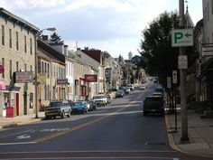 cars are parked on the street in front of some buildings and shops, with one car driving down the road