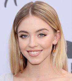 a woman with blonde hair and blue eyes smiles at the camera while wearing gold earrings