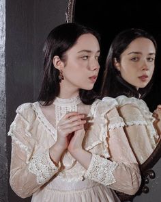 a woman standing in front of a mirror with her hands on her chest and looking at herself in the mirror