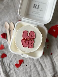 a cake in a box with two hearts on it and spoons next to it