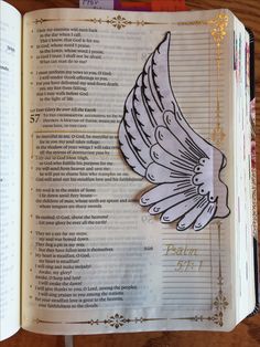 an open bible with the words and angel wings on it's side, sitting on a wooden table