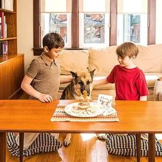 two boys and a dog are sitting at a table with food on it while the boy is eating