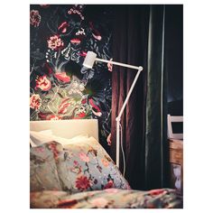 a bed with floral wallpaper and a white lamp on the headboard next to it