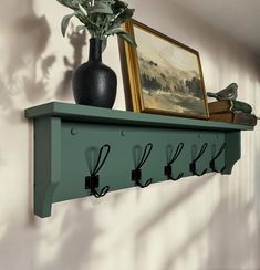 a green shelf with hooks on it next to a potted plant and framed painting