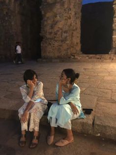 two women sitting on steps talking on their cell phones in front of an ancient building