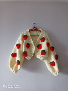 a white sweater with red and green cherries on it hanging from a hook against a wall