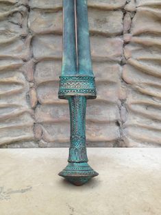 a blue vase sitting on top of a table next to a stone wall with a knife sticking out of it