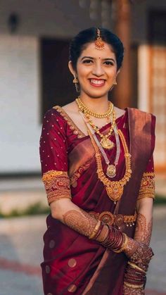 a woman in a maroon sari and gold jewelry smiling for the camera with her hand on her hip