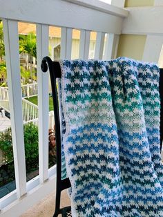 a blue and white crocheted blanket sitting on top of a black chair next to a balcony