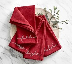 red napkins with embroidered names on them sitting on a white marble table top next to evergreen branches