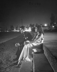 black and white photograph of two people sitting on a bench at night, one woman is looking off to the side