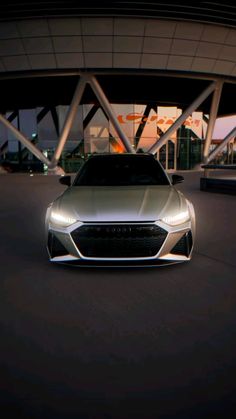 a silver car parked in front of a large building at night with its lights on