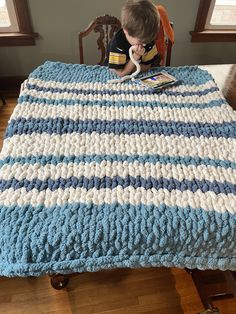 a young boy sitting on top of a bed next to a blue and white blanket