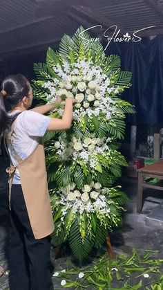 a woman is placing flowers on a large floral arrangement in the shape of a tree