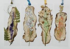 three pieces of altered paper with flowers and leaves on them, hanging from blue string