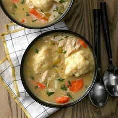 two bowls filled with chicken and dumplings next to spoons on a wooden table