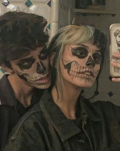 two people with face paint taking a selfie in a mirror together, one is holding a cell phone