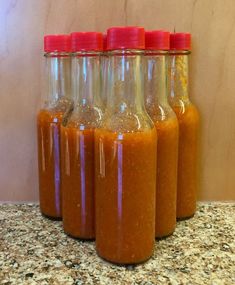 four jars filled with different kinds of sauce on top of a granite countertop next to a wall