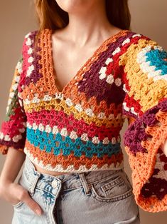 a woman wearing a multicolored crochet top and denim shorts with her hands in her pockets