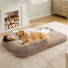 a woman laying on top of a dog bed next to a fire place