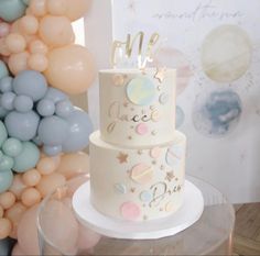 a three tiered cake sitting on top of a table with balloons in the background