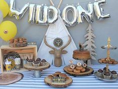 a table topped with cakes and desserts next to foil letters that spell out'wild one '