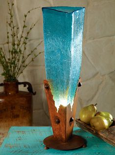 a tall blue vase sitting on top of a table next to some apples and flowers