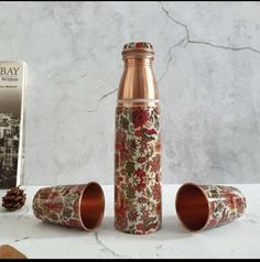 two copper cups and a book on a marble countertop next to an empty bottle