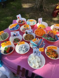 a table topped with lots of bowls filled with candy and candies on top of a pink table cloth