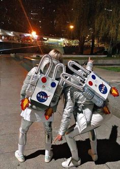 two people dressed as astronauts are standing on the sidewalk with their arms around each other