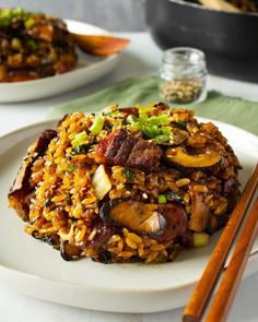 a white plate topped with fried food next to chopsticks and a bowl of rice