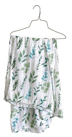 an off the shoulder top with green leaves on it hanging from a hanger, against a white background