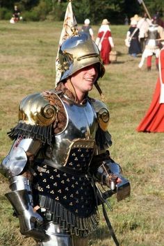 a man dressed in armor walking through a field with other men and women behind him