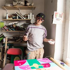 a man standing next to a table in a room filled with lots of clutter