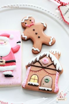 three decorated cookies on a plate with santa clause and gingerbread house in the background