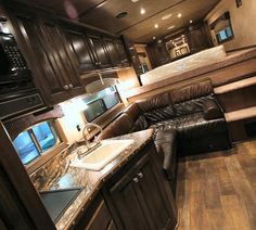 the interior of an rv with wood flooring and leather couches, kitchen area