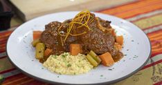 a white plate topped with meat and veggies next to mashed potatoes on a table