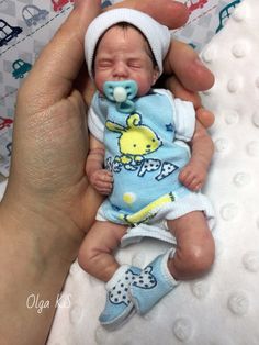 a hand holding a baby wearing a blue outfit