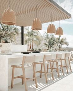 an outdoor kitchen with white counter tops and wooden chairs under a pergolated roof