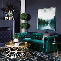 a living room with green velvet couches and gold coffee table in front of a fireplace