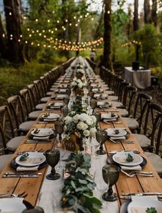 a long table set with plates and place settings for an outdoor dinner in the woods