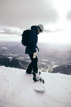 a snowboarder is standing on the top of a snowy hill with his board