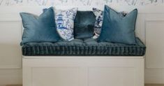 three blue pillows sitting on top of a white bench in front of a wallpapered wall