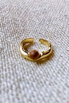 a close up of a gold ring on a white surface with a bead in the middle