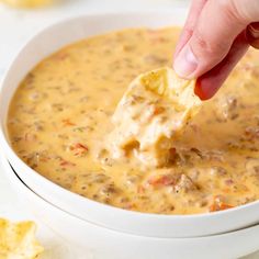 a hand dipping a tortilla chip into a bowl of quesadilla soup