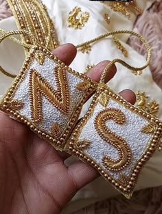 someone is holding two small gold and white embroidered squares with the letter s on them