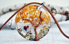 a glass pendant with an orange tree inside on a brown cord, sitting on a white surface